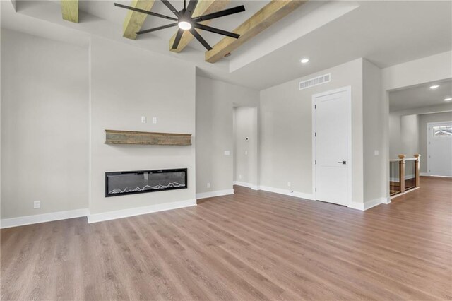 unfurnished living room featuring light wood-type flooring, ceiling fan, and beamed ceiling