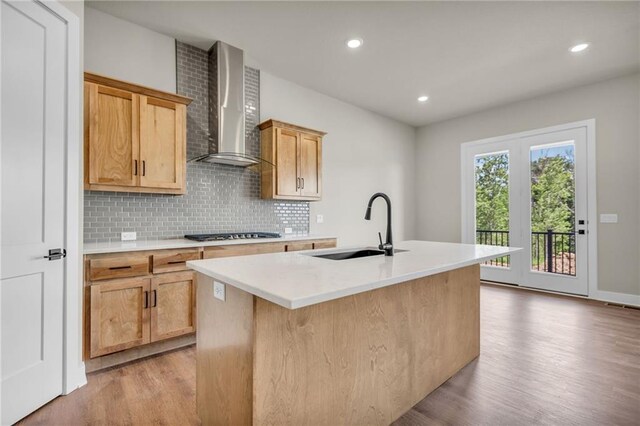 kitchen with light hardwood / wood-style floors, a center island with sink, wall chimney exhaust hood, and sink