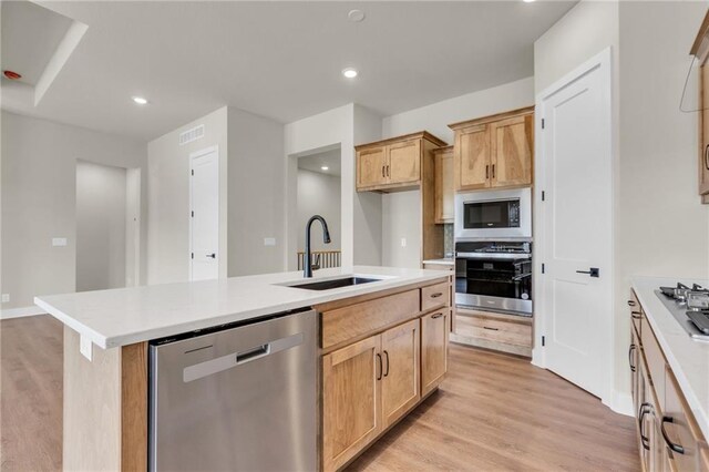 kitchen featuring light brown cabinets, sink, a kitchen island with sink, stainless steel appliances, and light wood-type flooring