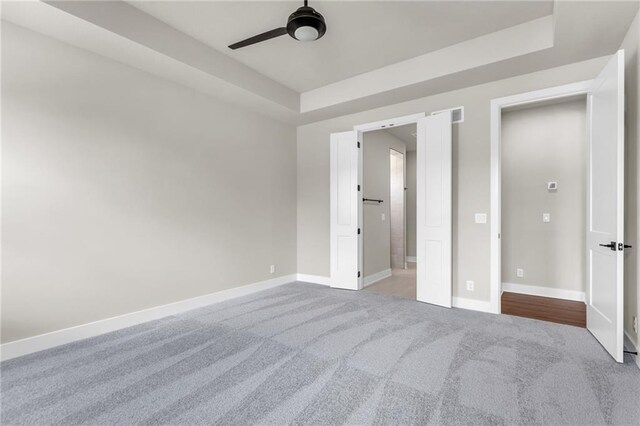 unfurnished bedroom featuring ceiling fan, light colored carpet, and a raised ceiling