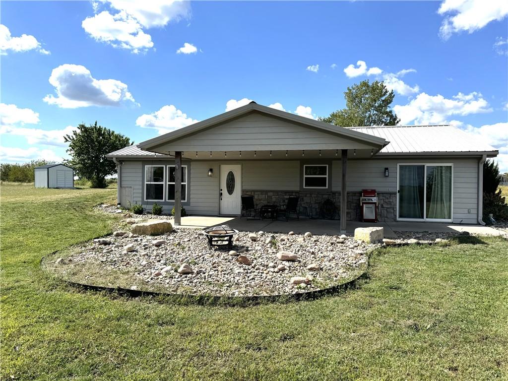 back of property with a shed, a fire pit, a yard, and a patio