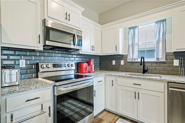 kitchen with white cabinetry, tasteful backsplash, light stone countertops, stainless steel appliances, and sink