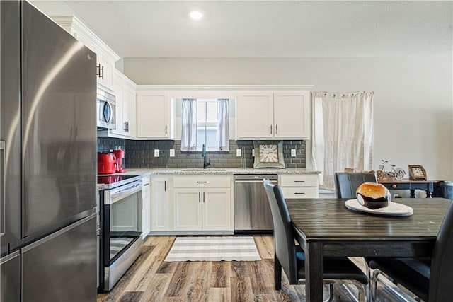 kitchen with white cabinetry, light hardwood / wood-style flooring, decorative backsplash, appliances with stainless steel finishes, and light stone countertops