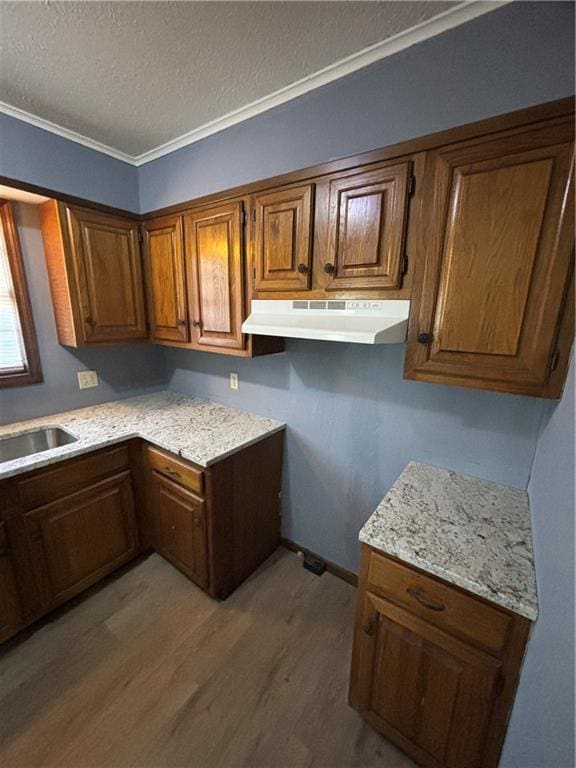 kitchen featuring sink, ornamental molding, light stone countertops, a textured ceiling, and hardwood / wood-style floors