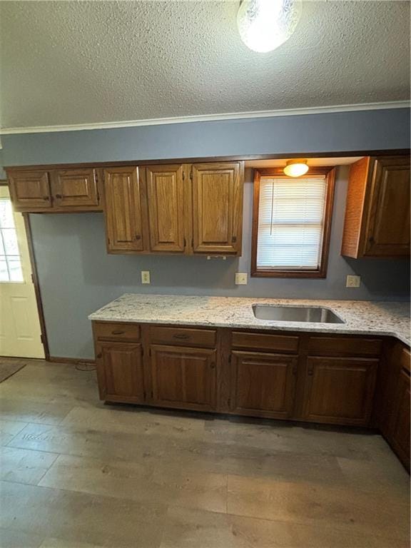 kitchen featuring a textured ceiling, sink, crown molding, and light hardwood / wood-style flooring