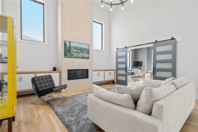 living room with an inviting chandelier, a barn door, light wood-type flooring, a fireplace, and a high ceiling