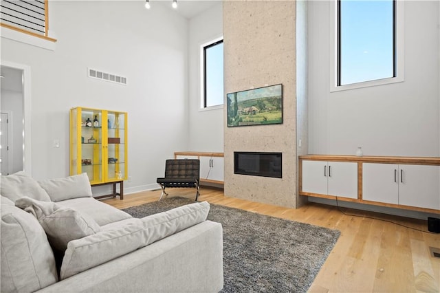 living room with a towering ceiling, a fireplace, and light hardwood / wood-style floors