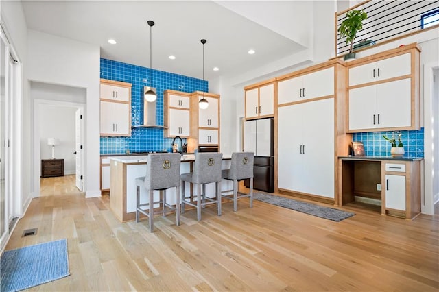 kitchen with pendant lighting, an island with sink, decorative backsplash, fridge, and light wood-type flooring