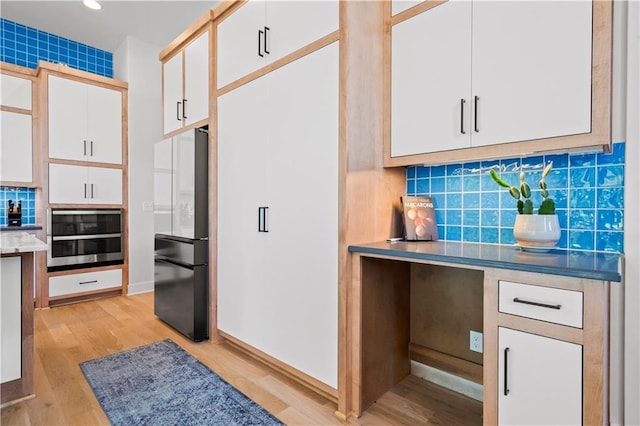 kitchen with white cabinets, fridge, stainless steel oven, and backsplash