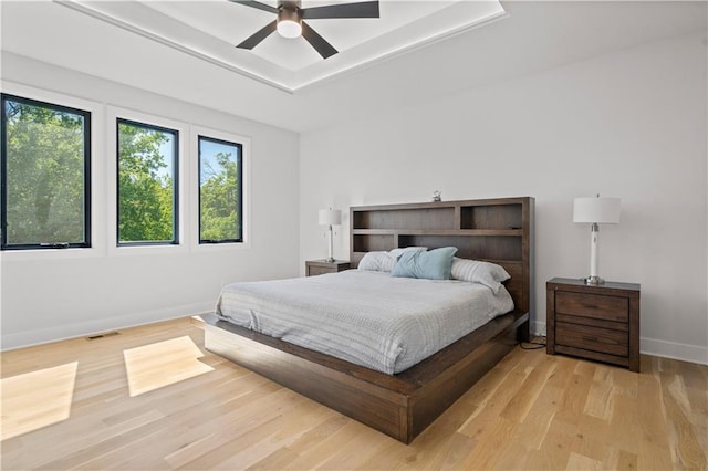 bedroom with light wood-type flooring, ceiling fan, and a tray ceiling