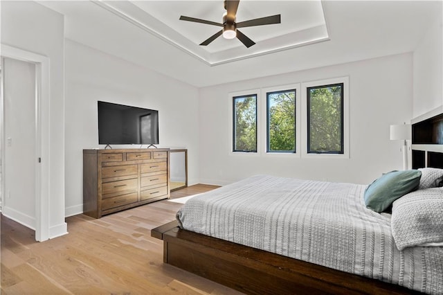 bedroom with ceiling fan, a tray ceiling, and light wood-type flooring