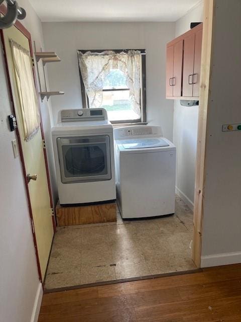 clothes washing area featuring washing machine and dryer, light hardwood / wood-style floors, and cabinets