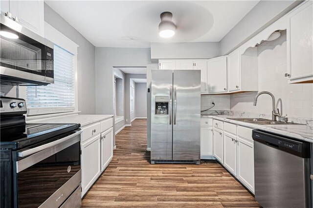 kitchen with appliances with stainless steel finishes, white cabinetry, tasteful backsplash, light stone countertops, and light wood-type flooring