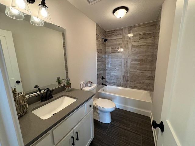 full bathroom featuring vanity, a textured ceiling, tiled shower / bath combo, and toilet