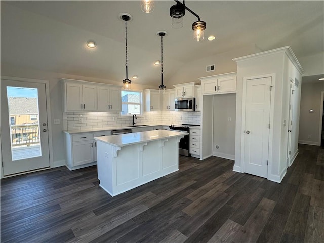 kitchen featuring appliances with stainless steel finishes, a sink, vaulted ceiling, white cabinets, and dark wood-type flooring