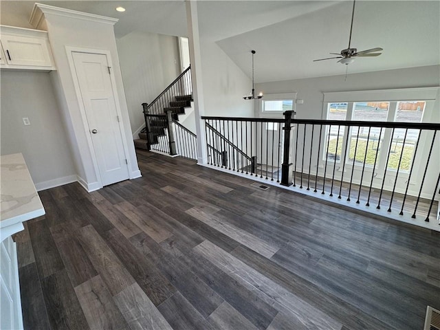 unfurnished living room with dark wood finished floors, baseboards, a ceiling fan, lofted ceiling, and a chandelier