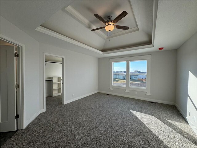unfurnished bedroom with a raised ceiling, carpet, a spacious closet, baseboards, and a ceiling fan