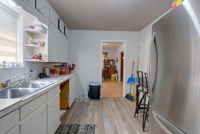 kitchen with sink, light hardwood / wood-style flooring, backsplash, white cabinetry, and stainless steel refrigerator