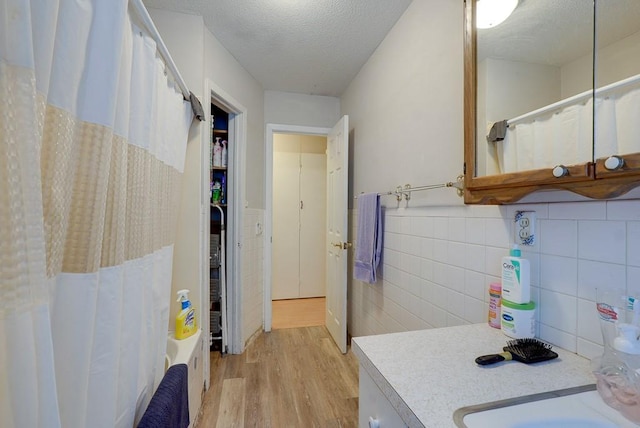 bathroom with shower / bath combination with curtain, vanity, a textured ceiling, hardwood / wood-style flooring, and tile walls