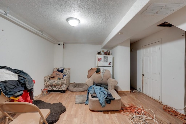 basement featuring a textured ceiling, hardwood / wood-style flooring, and white refrigerator