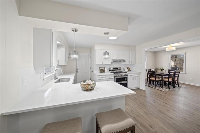 kitchen with a kitchen breakfast bar, kitchen peninsula, sink, stainless steel gas stove, and white cabinetry