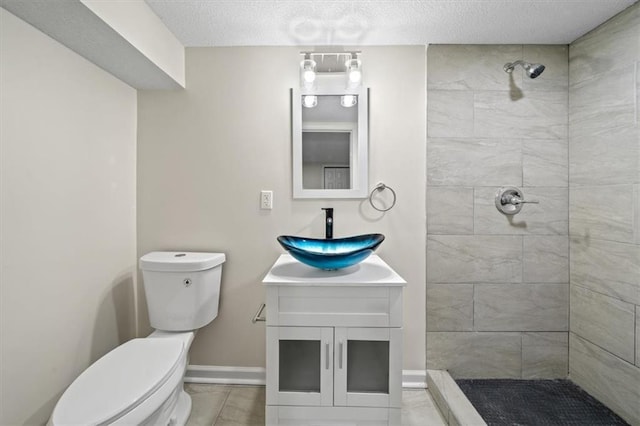 bathroom with a tile shower, vanity, a textured ceiling, tile patterned flooring, and toilet