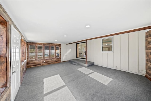 unfurnished living room featuring carpet flooring, wood walls, and ornamental molding