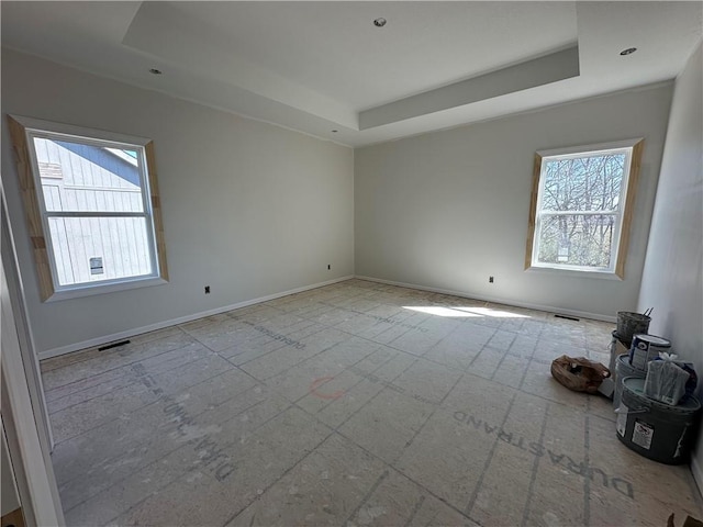 unfurnished room with a tray ceiling, baseboards, and visible vents