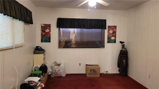 interior space with carpet, wood walls, and ceiling fan