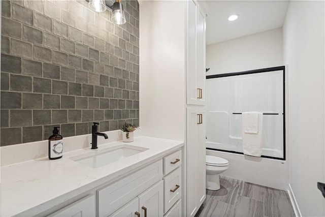 full bathroom with decorative backsplash, toilet, vanity, and combined bath / shower with glass door