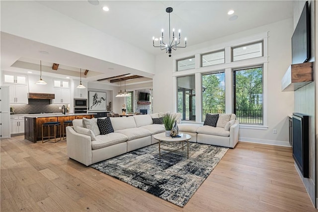 living room featuring a chandelier, light hardwood / wood-style floors, a tray ceiling, sink, and a fireplace