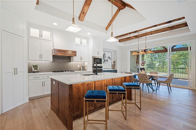 kitchen with pendant lighting, a kitchen island with sink, light wood-type flooring, and white cabinetry