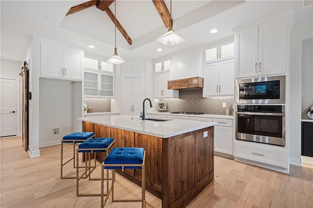 kitchen with light wood-type flooring, hanging light fixtures, decorative backsplash, stainless steel appliances, and a center island with sink