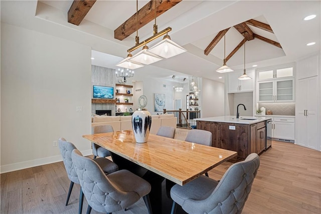 dining area featuring vaulted ceiling with beams, light hardwood / wood-style floors, a chandelier, and sink