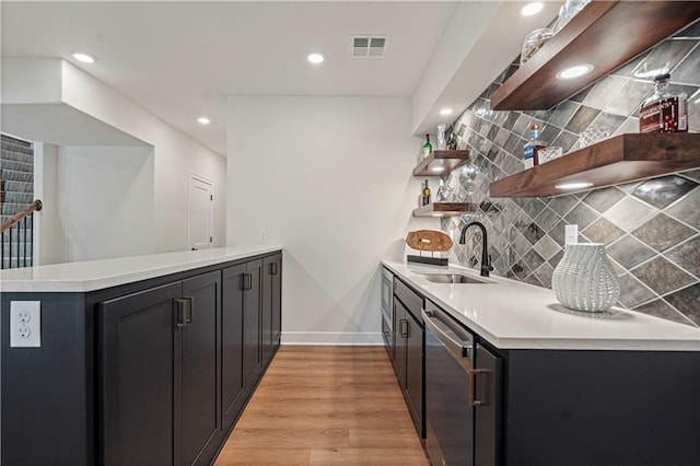 kitchen with light wood-type flooring, dishwasher, sink, kitchen peninsula, and backsplash