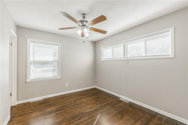 empty room featuring ceiling fan, a textured ceiling, plenty of natural light, and dark hardwood / wood-style flooring