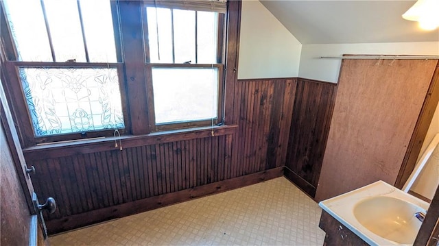 bathroom featuring vanity, wood walls, and vaulted ceiling