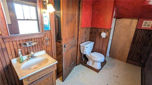 bathroom featuring wooden walls, vanity, and toilet