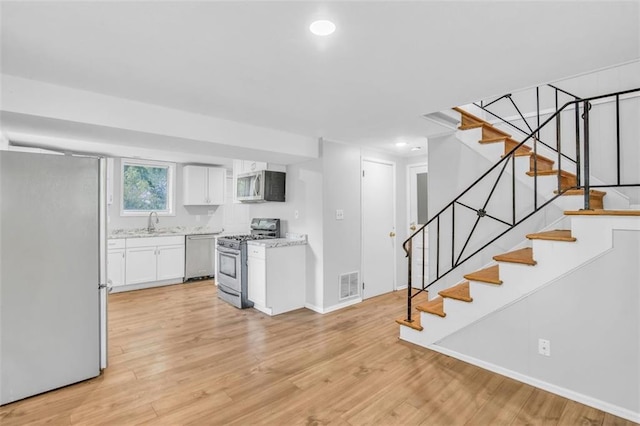 kitchen with stainless steel appliances, white cabinets, light wood-type flooring, and sink