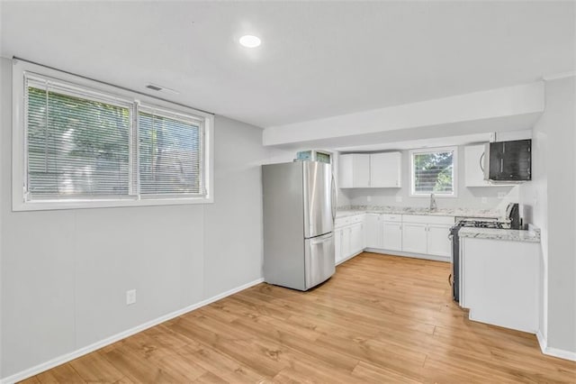 kitchen featuring white cabinetry, stainless steel refrigerator, light wood-type flooring, stove, and sink