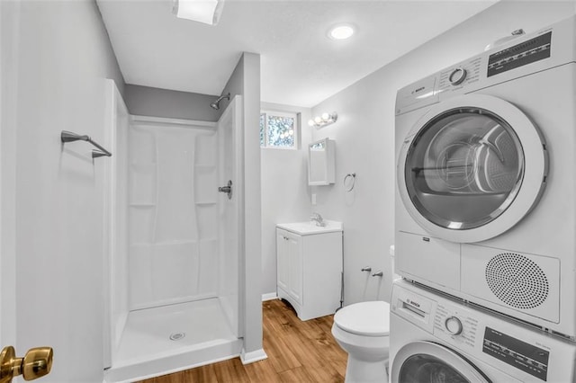 bathroom featuring vanity, toilet, hardwood / wood-style floors, walk in shower, and stacked washer and dryer