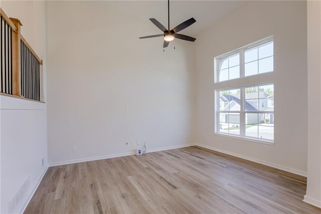 unfurnished room with a high ceiling, ceiling fan, and light hardwood / wood-style flooring