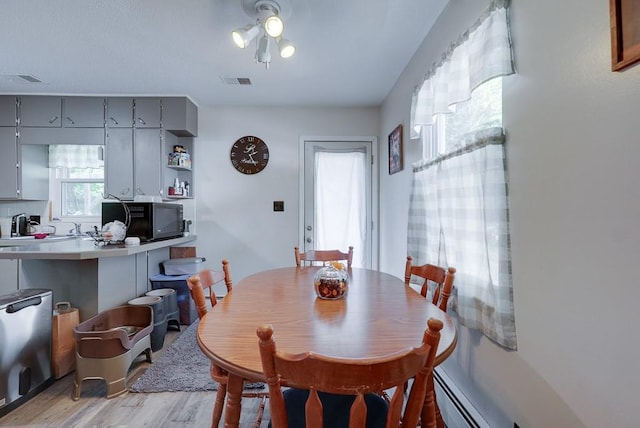 dining area featuring visible vents, a baseboard radiator, and light wood-style flooring