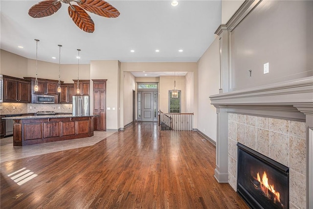 kitchen featuring appliances with stainless steel finishes, a tiled fireplace, a kitchen island with sink, and dark hardwood / wood-style flooring