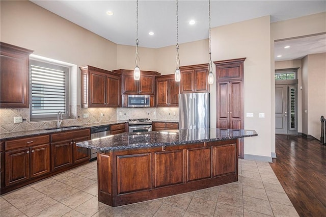 kitchen with pendant lighting, dark stone counters, sink, appliances with stainless steel finishes, and a center island