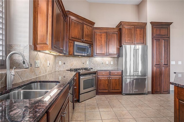 kitchen with appliances with stainless steel finishes, dark stone countertops, sink, and light tile patterned flooring