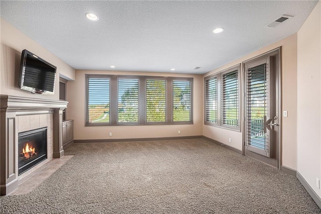 unfurnished living room with light colored carpet, a tile fireplace, and a textured ceiling