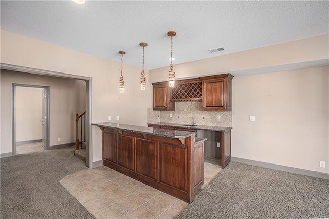 kitchen with dark stone counters, light colored carpet, backsplash, kitchen peninsula, and hanging light fixtures