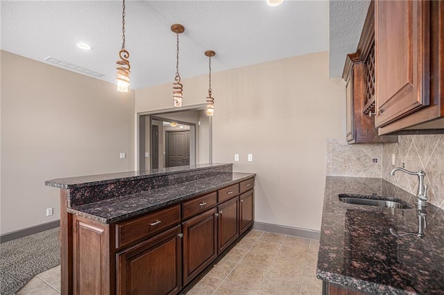 kitchen featuring pendant lighting, dark stone countertops, sink, kitchen peninsula, and a textured ceiling