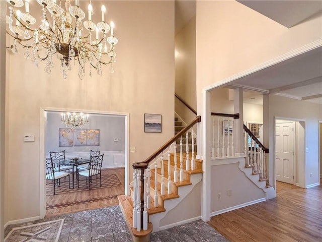 staircase featuring wood-type flooring, a towering ceiling, and an inviting chandelier